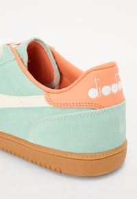 Mint green suede sneaker with white accents, coral heel, and textured gum sole. Features brand logo in white on the heel.