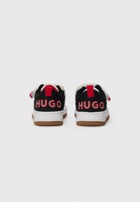 Baskets noires avec des accents rouges, présentant une tige en mesh texturé et une semelle blanche. "HUGO" en lettres rouges en relief à l'arrière.