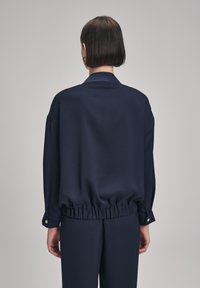 Marinblus med avslappnad passform, elastisk nederkant och knappade manschetter, tillverkad i ett slätt tyg med mjuk textur.