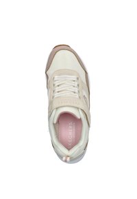 Beige en witte Skechers sneaker met klittenbandsluiting, veters en een roze traagschuimzool, bekeken van bovenaf op een witte achtergrond.