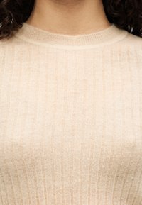 Φως μπεζ πλεκτό πουλόβερ με ριμπ υφή και στρογγυλή λαιμόκοψη, με απαλό, ελαφρύ ύφασμα και διακριτικές διακυμάνσεις στο χρώμα.