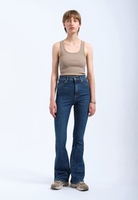 Brown ribbed tank top paired with high-waisted blue flared jeans and tan sneakers, set against a plain white background.