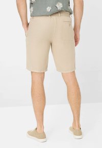 Pantaloni corti in cotone beige con una finitura testurizzata, dotati di una tasca posteriore e orli arrotolati, abbinati a scarpe casual beige.