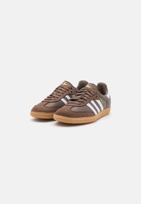 Braune Sport-Sneaker mit einem Obermaterial aus glattem Leder und Wildleder, weißem Drei-Streifen-Design und einer Sohle aus Gummirubber. Gold-Akzent auf der Zunge.
