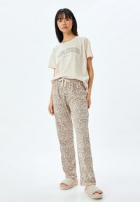 Beige graphic t-shirt met korte mouwen, gecombineerd met gemêleerde lichtbruine loungebroeken met een trekkoord in de taille en zachte, donzige slippers.