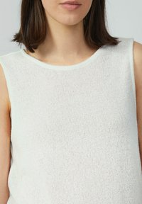 Débardeur blanc sans manches en tissu tricoté texturé, avec un col rond et une coupe douce, légèrement ample. Pas de motifs ou d'accents visibles.