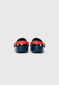 Blue rubber clogs with a red heel strap, featuring ventilation holes and a textured sole. Branding is visible on the side of the strap.