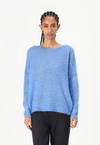 Μπλε, υπερμεγέθης πουλόβερ από μαλακό, φουντωτό υλικό με φαρδύ λαιμό και ελαφρώς κοντό στρίφωμα, συνδυασμένο με μαύρα παντελόνια.