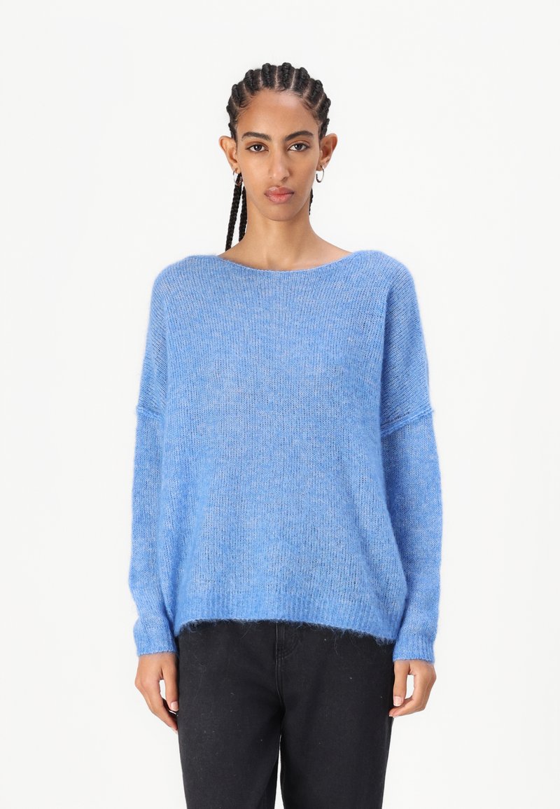 Μπλε, υπερμεγέθης πουλόβερ από μαλακό, φουντωτό υλικό με φαρδύ λαιμό και ελαφρώς κοντό στρίφωμα, συνδυασμένο με μαύρα παντελόνια.