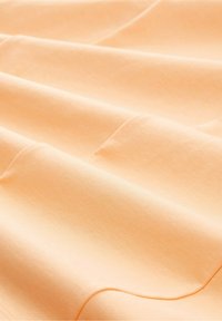 Tissu de couleur pêche avec une surface lisse et légèrement texturée, présentant de doux plis et un éclat subtil à la lumière naturelle.