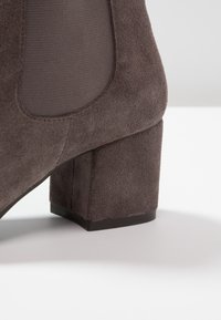 Botte de cheville en suède marron avec un talon carré, dotée de panneaux latéraux en élastique pour plus d'aisance et d'une doublure en tissu lisse.