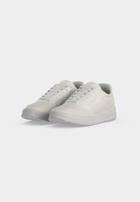 Paire de baskets basses blanches avec fermeture à lacets et semelles souples texturées sur fond clair.