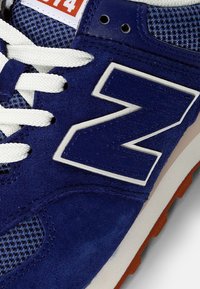 Blå sneakers med en texturerad mockaöverdel, mesh-paneler, vita snören, en framträdande vit "Z"-logotyp, och en kontrasterande orange etikett.