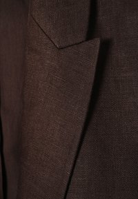 Gros plan sur un tissu brun foncé texturé montrant le revers net d'une veste ou d'un blazer sur mesure.