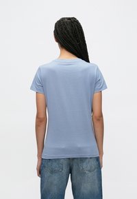 Ανοιχτό μπλε βαμβακερό μπλουζάκι με στρογγυλή λαιμόκοψη και κοντά μανίκια, με ομαλή υφή και κανονική εφαρμογή, συνδυασμένο με τζιν παντελόνι.