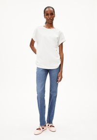 Witte korte mouw shirt met opgerolde mouwen, gecombineerd met lichtblauwe slim-fit jeans en lichtroze schoenen met uitsparingen.
