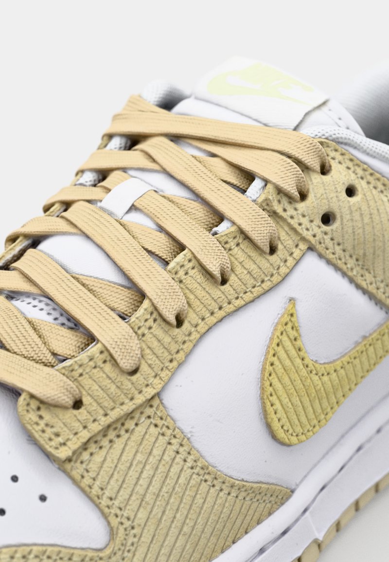 Nike-Sneaker mit einer weißen Lederbasis und gelben Cordura-Akzenten, strukturierten Paneelen und beigen Schnürsenkeln. Dezentes Logo-Detail an der Seite.