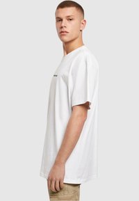 T-shirt en coton blanc avec une coupe décontractée, présentant des manches courtes et un col rond, affichant un texte noir minimal sur le devant.