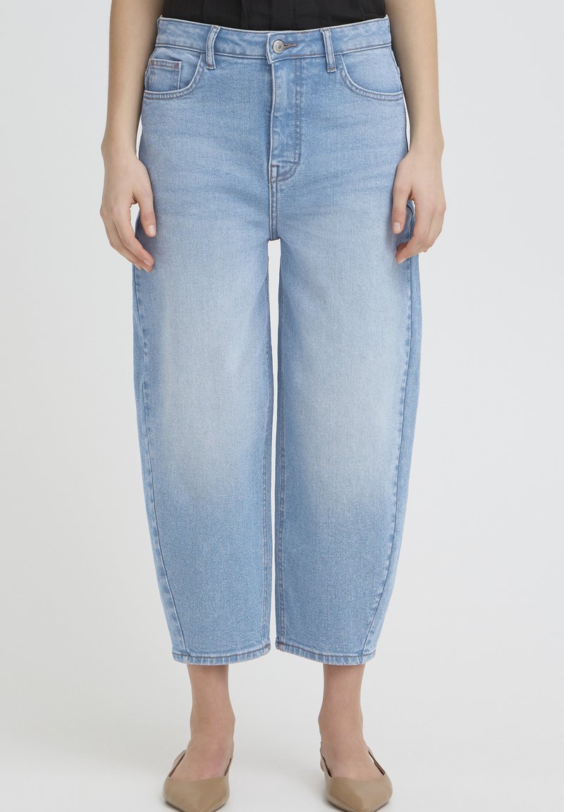 Vaqueros azul claro de talle alto con un ajuste cómodo. Presentan bolsillos frontales, trabillas para cinturón y una textura ligeramente descolorida. El dobladillo termina por encima del tobillo.