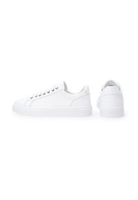 Hvide canvas sneakers med en rund tå, flade snørebånd og en tekstureret gummisål. Har et minimalistisk design og rene, glatte overflader.
