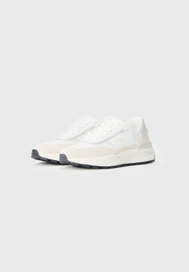 Witte sportieve sneakers met een mix van gladde en textuurmaterialen, met een grijze rubberen zool en een gewatteerde enkelkraag.