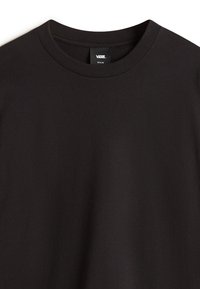 Camiseta de algodón negra con cuello redondo, con una textura suave y una pequeña etiqueta de la marca en el interior del cuello. Tamaño mediano.