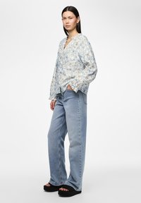 Blouse légère à motifs floraux, bleu clair, avec des manches longues et une patte de boutonnage, associée à un jean en denim clair, taille haute, à jambe droite.