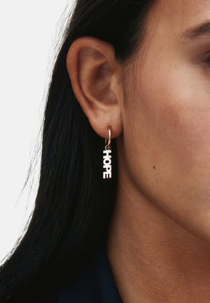 Guldørering med hul form, der har ordet "HOPE" i fede, hvide bogstaver. Designet er moderne med en glat, poleret overflade.