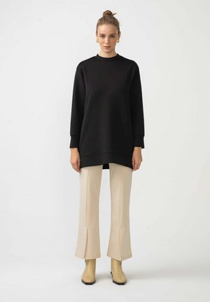 Black oversized sweatshirt with long sleeves, worn over light beige flared pants with side slits, paired with ankle-height yellow boots.