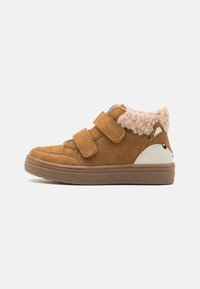 Brune semskede høje sneakers med to velcro-remme, fluffy beige krave og hvid hælaccent med et tegneserieansigt design.