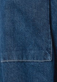 Mörkblå denimtyg med en synlig söm och struktur. Materialet verkar något blekt med en mjuk, vävd yta.