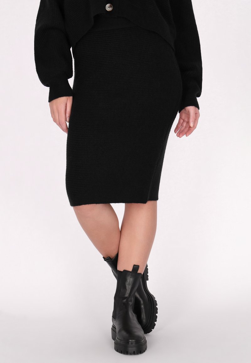 Zwarte gebreide rok met een aansluitende vorm en ribbeltextuur, gecombineerd met zwarte leren enkellaarzen met een chunky zool en een trekband.