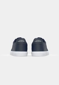 S ténis de pele azul-marinho com solas de borracha brancas, apresentando o logo da Lacoste na aba do calcanhar e um design liso e minimalista.