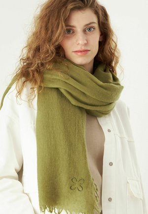 Olijfgroene sjaal gemaakt van zachte, gestructureerde stof, met subtiele bloem borduursels en franjes aan de randen, gedragen over een beige top.