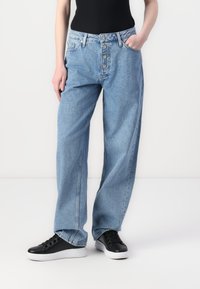 Light blue denim jeans with a relaxed fit, five-button fly, and two front pockets, paired with black sneakers on a plain background.