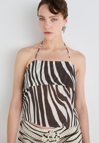Smeđi i krem halter top s slojevitim dizajnom koji uključuje zebra pruge. Lagana tkanina s glatkom teksturom.