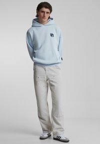 Felpa con cappuccio azzurro chiaro con tasca frontale e logo ricamato, abbinata a pantaloni cargo beige con multiple tasche e vestibilità dritta.
