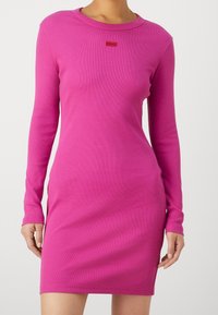 Úzké šaty s dlouhým rukávem v sytě růžovém žebrovaném materiálu. Disponují kulatým výstřihem a malým červeným logem na hrudi.