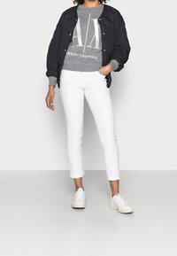 Svart quiltad bomberjacka, grå sweatshirt med vitt tryck, vita slim-fit jeans och vita sneakers. Texturerade material och avslappnad design.