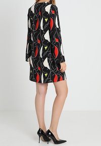 Mustapituinen pitkähiha dressi, jossa on abstrakteja punaisia, keltaisia ja valkoisia kuvioita. Sujuva kangas, polvipituinen, yhdistetty mustiin korkokenkiin.