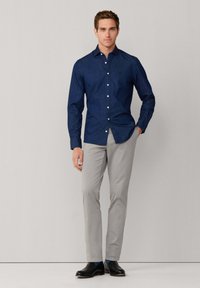Ciemnoniebieska koszula z długim rękawem, połączona z jasnoszarymi dopasowanymi spodniami oraz czarnymi eleganckimi butami. Gładki materiał, klasyczny krój kołnierzyka.
