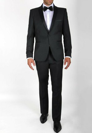 Costume noir avec revers en satin, chemise blanche et nœud papillon noir. Design simple, coupe ajustée et chaussures noires brillantes.