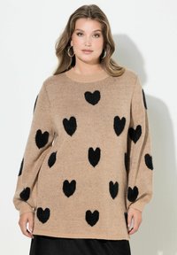 Maglione beige con grandi motivi a cuore neri. Ha una scollatura rotonda, maniche lunghe e un tessuto morbido e strutturato.