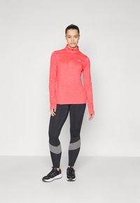 Långärmad rosa träningströja med en kvarts dragkedja, parat med svarta leggings med grå detaljer. Båda är gjorda av texturerade, stretchiga material.