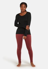 Top negro de manga larga con escote redondo combinado con leggings burdeos. Ambas prendas son ajustadas y están hechas de una tela suave y elástica.