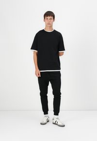 Schwarzes T-Shirt mit kurzen Ärmeln und weißen Akzenten, kombiniert mit schwarzen Jogginghosen und weißen Sneakers mit schwarzen Streifen. Einfaches, lässiges Design.