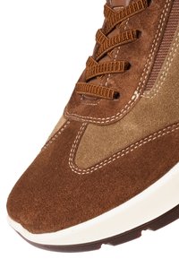 Brown suede sneaker with light brown accents, detailed white stitching, and brown woven laces on a white rubber sole.