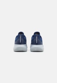 Niebieskie buty sportowe z siateczkową cholewką, wyściełanym kołnierzem i białą podeszwą środkową z teksturowaną podeszwą z gumy. Nazwa modelu "GAMECOURT 2" wyświetlona.