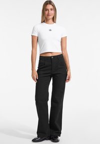 Crne široke hlače od blago teksturirane tkanine, u kombinaciji s bijelom skraćenom majicom koja ima mali grafički print zvijezde.