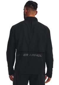 Giacca leggera nera con colletto alto e design a strati sul retro. Presenta il logo riflettente "UNDER ARMOUR" sulla parte posteriore.